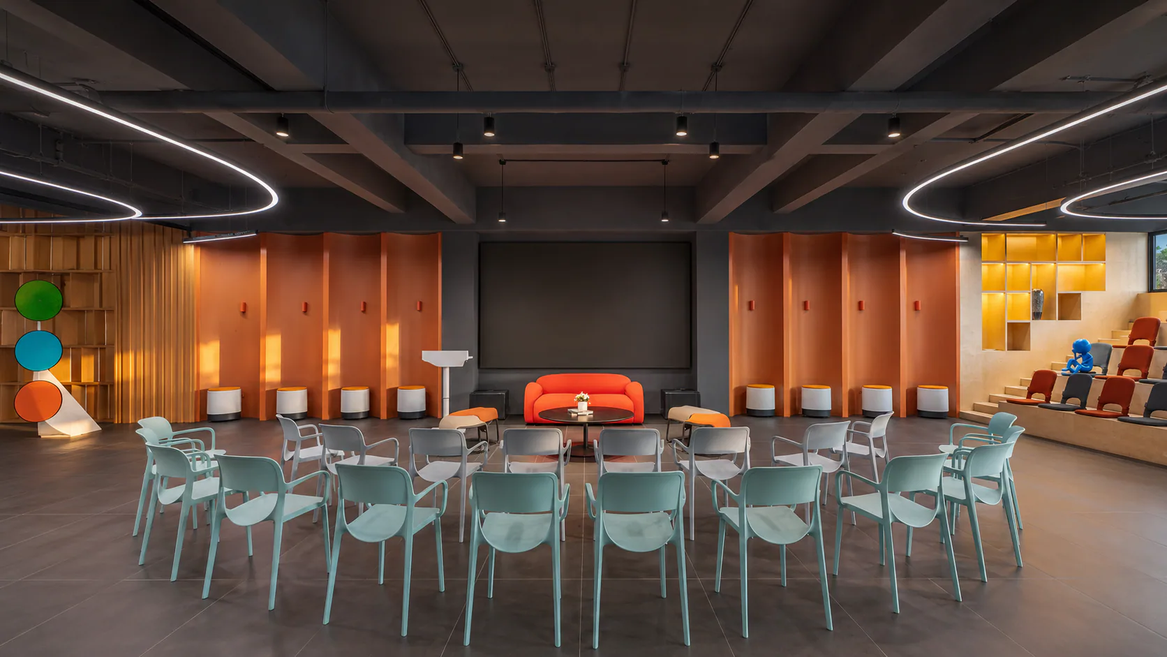Presentation area with rows of chairs, a central screen and curved ceiling lights.