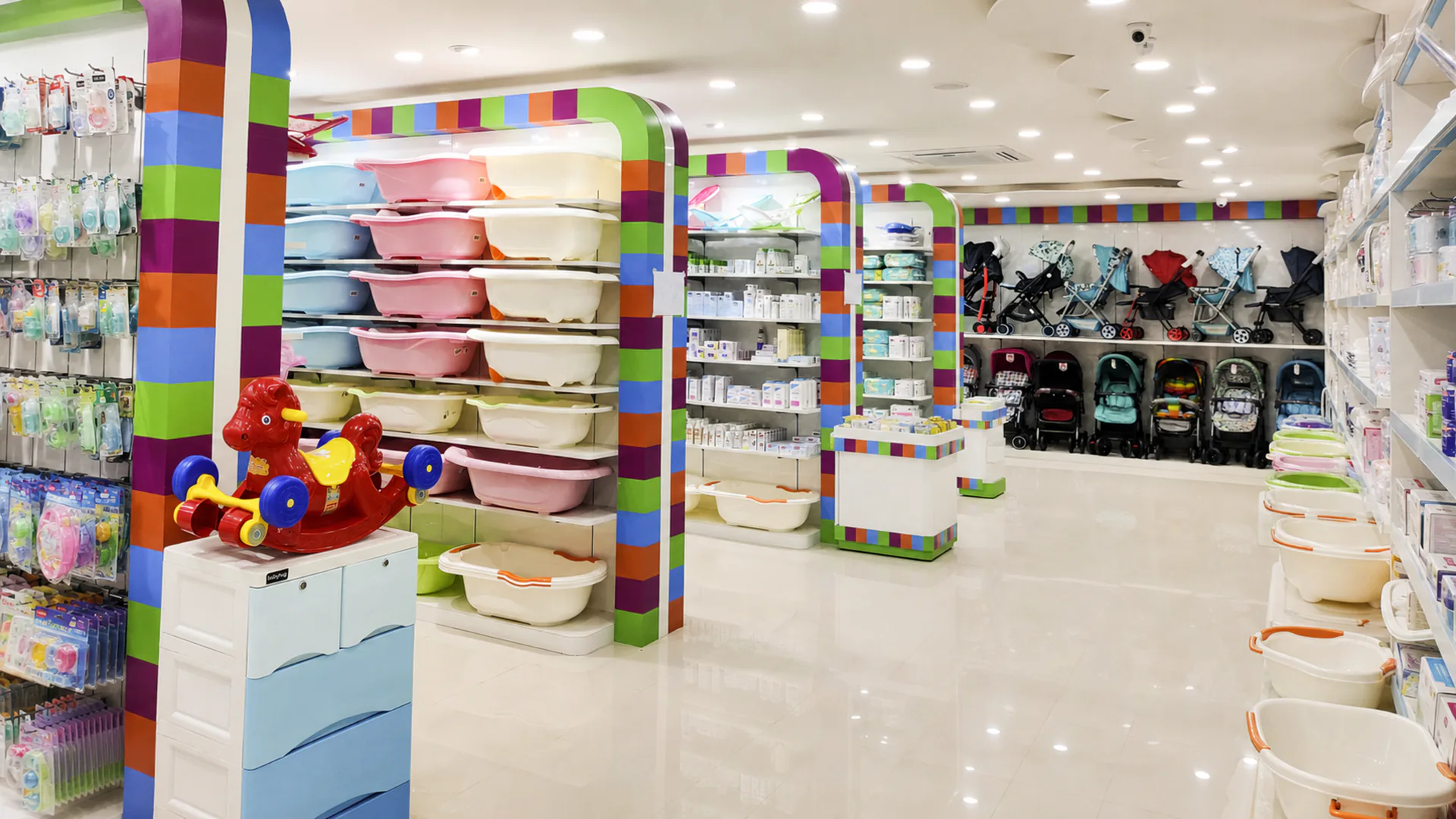 Interior aisle with baby bath products, accessories and strollers arranged within colourful rounded display frames.