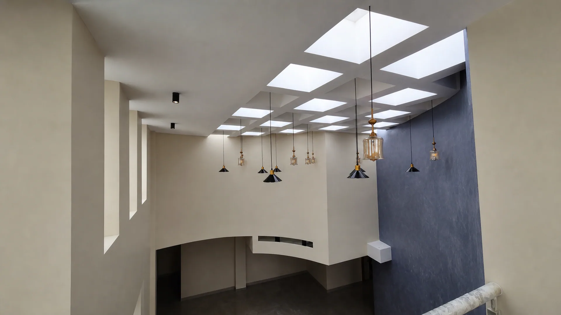 Double-height stair void with geometric ceiling openings and pendant lights.